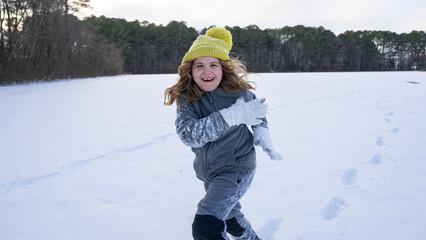 Winter snowball fight in the park. Kid plays joyfully in snowfall. Winter kids portrait. Snowflakes...