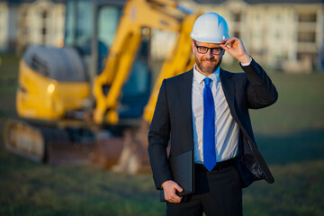 Construction builder manager or supervisor at a construction site. Portrait of construction manager worker in hardhat and suit near excavator. Renovation with construction manager or supervisor.