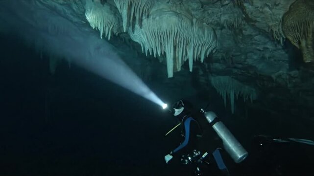 A mysterious shot of a cave diver exploring a crystal-clear underwater cavern, with a powerful light beam revealing ancient rock formations.
