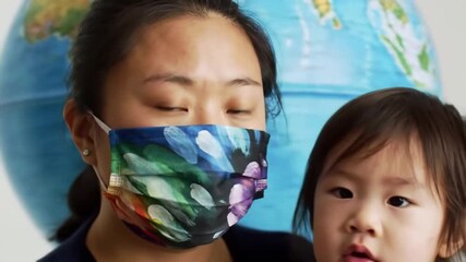 Asian mother  child with floral mask with globe background Pandemic era family. - Powered by Adobe