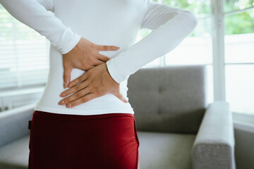 Obraz premium A woman experiences back pain, holding her lower spine in discomfort. The image highlights health problems, poor posture, muscle strain, stress, and the need for treatment, therapy, and care.