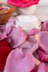 Container with skin care cream surrounded by pink and red flower petals, vertical shot
