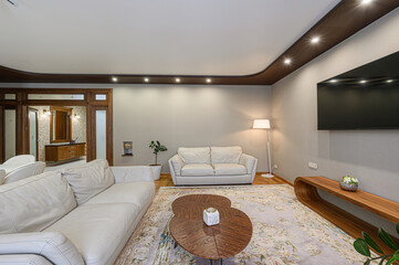 modern living room features white sofas, a patterned rug, a wood coffee table, and a large TV....