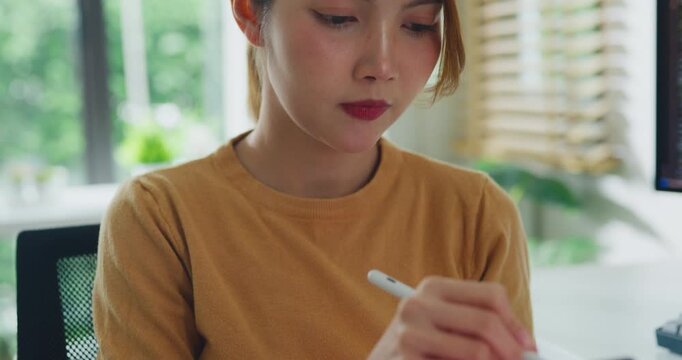 Closeup young Asia female freelance write code on tablet while work prompt AI IT app smart program nomad, video game, terminal coding, user interface, data center on desktop computer at home office.