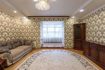 cozy room with patterned wallpaper, a sofa, and a dark wood cabinet. A round rug anchors the space, which features a view into a bright, windowed area