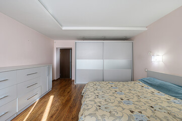 cozy bedroom with a floral bedspread, light pink walls, a white sliding-door closet, and a matching dresser on wood floors