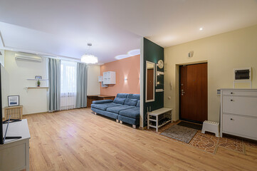 modern apartment living room featuring a blue sofa, wooden floors, and a distinct entrance area