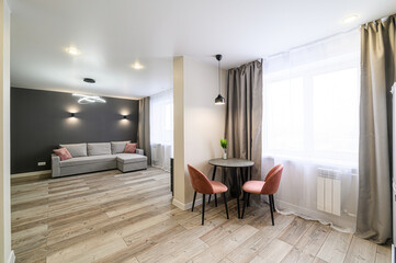Modern apartment interior with a gray sofa, round table, and pink chairs.  Bright, airy space with wood-look flooring