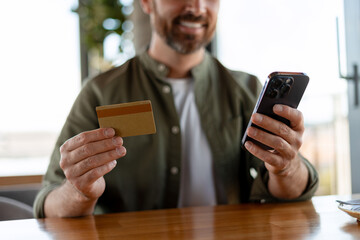 Smiling man making online payment using credit card and smartphone