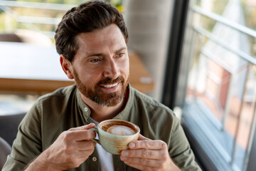 Happy businessman drinking cappuccino and looking outside during a coffee break