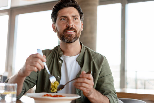 Man eating pasta looking up in modern restaurant