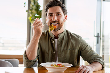 Smiling man eating pasta in restaurant enjoying healthy meal