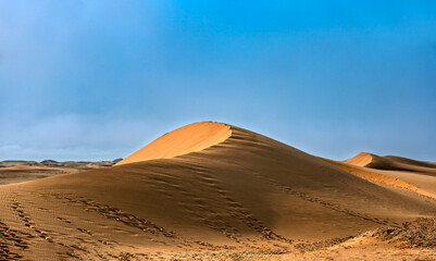 Namibia sand dunes with footsteps, clue sky with sun and clouds , on empty barren landscape, hot day