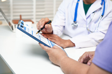 A male Asian doctor checks on an obese female patient at a desk, addressing her high blood...