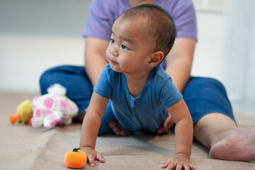 An Asian aunt joyfully spends time with her 1-year-old nephew in a cozy living room. They smile,...
