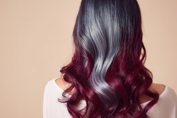 Naklejka premium A woman's back view showcases vibrant, multi-toned, wavy hair with a captivating ombre effect of burgundy and silvery gray hues against a neutral backdrop.