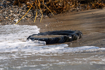 A tractor wheel thrown away on the seashore. Plastic pollution. Environmental pollution.