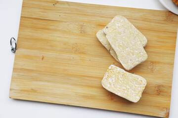 Slices of raw tempeh on a clean wooden cutting board. A healthy, plant-based protein and staple of Indonesian cuisine, ready for cooking.