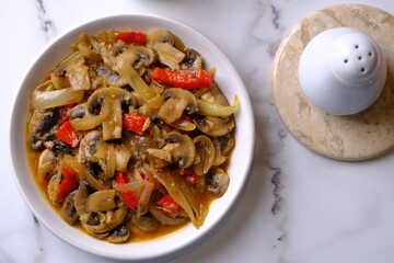 champignon mushrooms, onions, and red bell peppers cooked with black pepper in a white ceramic dish.