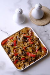 champignon mushrooms, onions, and red bell peppers cooked with black pepper in a white ceramic dish.