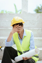 Female construction worker in hard hat and safety vest looking stressed, highlighting workplace...