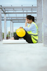 Female construction worker in hard hat and safety vest looking stressed, highlighting workplace...