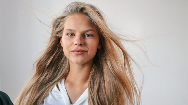 Confident young woman with long blonde hair and natural makeup looking at camera, wearing white blouse, fresh beauty and lifestyle portrait with dynamic hair