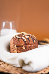 A round chocolate bread topped with almond slices, placed on a white cloth over a woven mat, surrounded by simple props on a dark background.