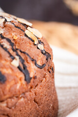 A round chocolate bread topped with almond slices, placed on a white cloth over a woven mat, surrounded by simple props on a dark background.