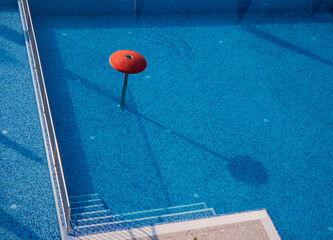 Empty outdoor swimming pool with blue mosaic tiles, steps, and red water fountain structure in the...