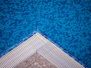 Swimming pool corner with blue mosaic tiles and water drainage grid.
