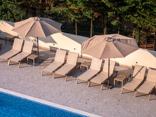 Row of sun loungers with large umbrellas by a swimming pool, outdoor relaxation area at resort or...