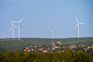 Four wind turbines on a hill above a rural village, generating renewable energy with green fields...