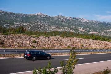Black car driving on highway with mountain range in background. Asphalt road with guardrails and...