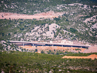 Concrete highway viaduct built into rocky mountain slope with green vegetation. Modern road...