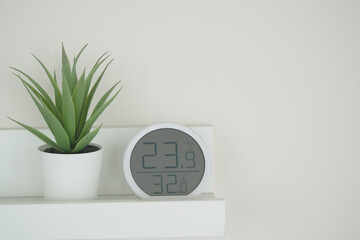 A sleek digital clock displays temperature and humidity beside a small plant
