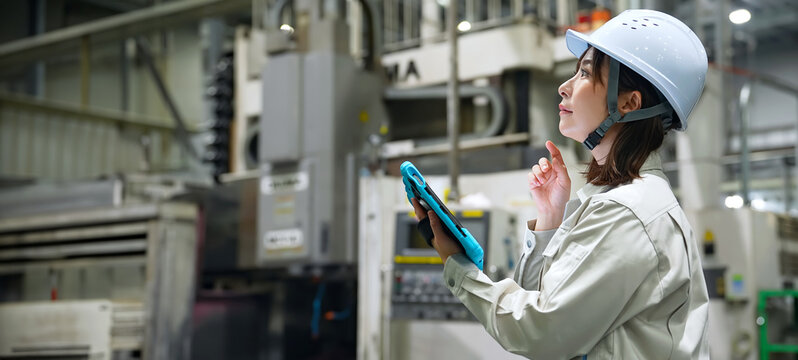 A female worker inspecting factory machinery with a tablet