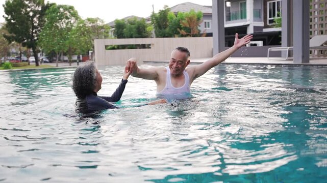 Asian Senior man and woman celebrating life in a swimming pool. Elderly Couple splashing water joyfully while laughing at heathy club.