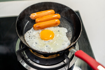 A hand expertly flips sausages in a hot pan while perfectly fried eggs cook alongside them....