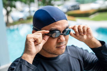 A person in a dark swim cap and rash guard adjusts their swimming goggles ready to dive into the pool. Aquatic sports and a healthy active lifestyle perfect fitness and summer activities.