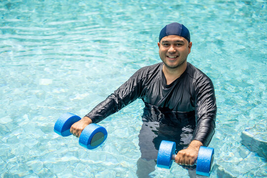 A smiling person in a swim cap and rash guard is submerged in a pool, holding blue aquatic dumbbells. This image captures the essence of hydrotherapy and a refreshing water workout.