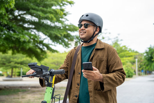 Young Asian man rent the scooter EV scan by smartphone. Sustainable save energy lifestyle. Commute and carbon neutral transportation. Asian tourist man put on helmet ride the scooter EV