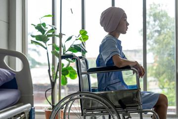 A cancer patient sits in a wheelchair with an IV drip looking stressed and sad. Asian Woman...