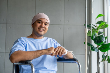 A male cancer patient in a wheelchair with an IV smiles with joy and hope showing strength and...