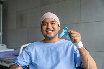 A male cancer patient sits in wheelchair with IV drip holding a blue ribbon symbolizing prostate...