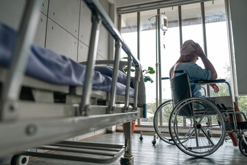 Obraz premium Asian male cancer patient sits in a wheelchair with an IV drip stress and sadness reflecting the emotional burden of illness. Man receiving IV treatment in a wheelchair looking tired and depressed