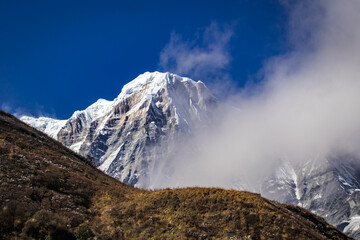 Annapurna South mountain peak in Nepal Himalaya partly covered by clouds under clear blue sky