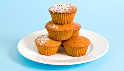 A stack of golden cupcakes rests on a white plate, dusted with powdered sugar, against a light sky-blue backdrop.