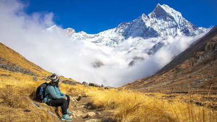Hiker Resting on trekking trail looking at snow covered Mt. Fishtail or machapuchhre mountain of Nepal himalaya. Majestic Mountain Landscape Above Clouds Adventure