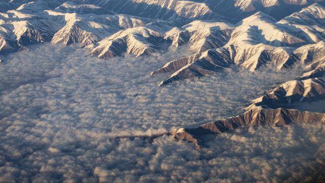 Aerial view of snow-covered Himalayan hindu kush mountain peaks with dense cloud cover filling the deep valleys at sunrise